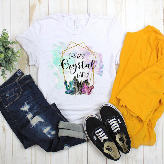 Crazy Crystal Lady Sublimation Transfer, white T-shirt with colorful crystal and watercolor design and text, paired with ripped jeans, yellow jacket, and black Vans sneakers on wooden floor.