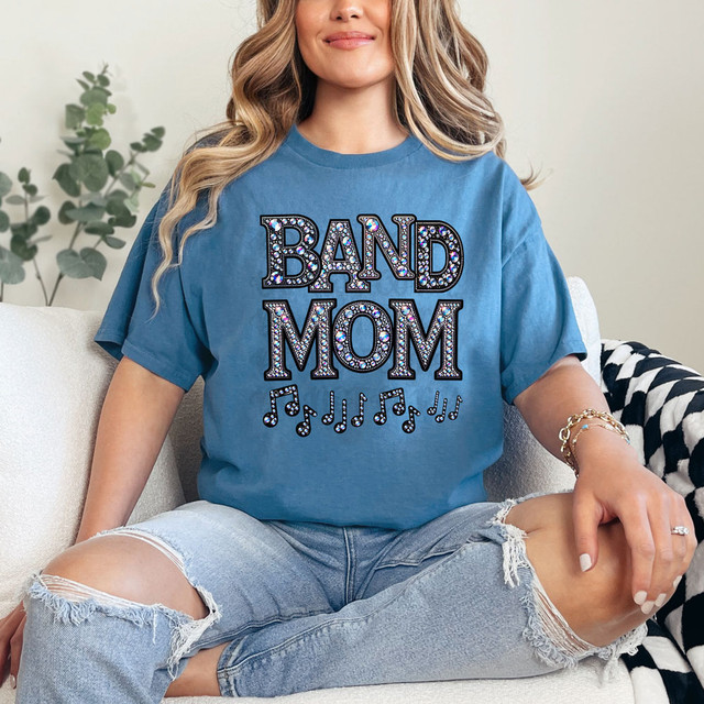 Band Mom Faux Rhinestone DTF Heat Transfer, a close-up of a woman wearing a blue T-shirt with a rhinestone-embellished 'BAND MOM' design and musical notes, showcasing the product's sparkling rhinestone details.
