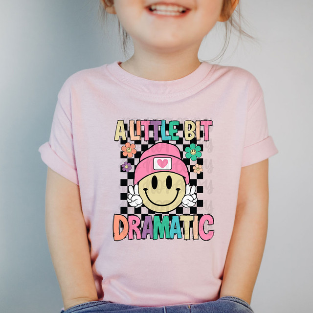 Little Bit Dramatic DTF Heat Transfer on a girl's pink T-shirt, featuring a comic-style smiley face wearing a pink beanie and surrounded by colorful flowers.