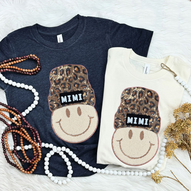 Mimi Beanie Happy Face Sequin Patch, two t-shirts featuring a smiley face design with leopard print beanie, surrounded by beaded necklaces and dried flowers.