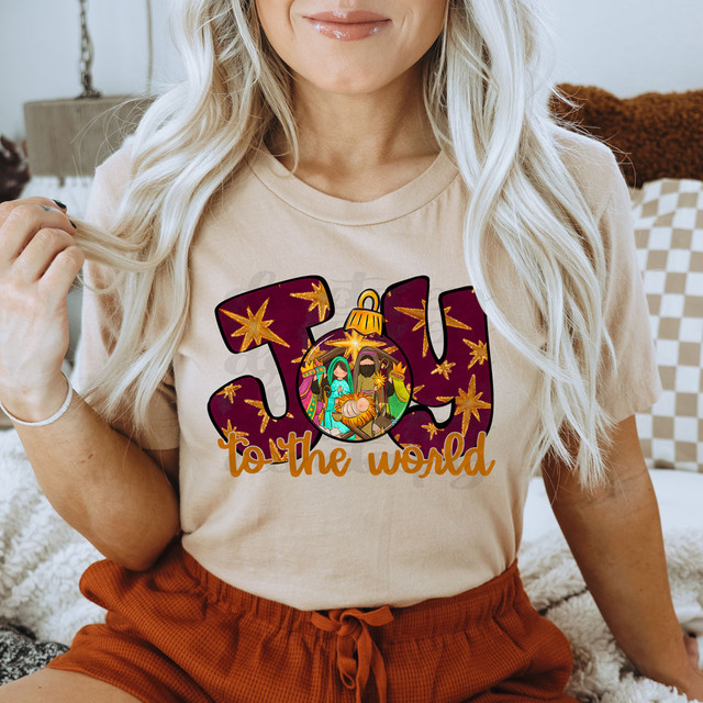 Joy To The World Nativity Scene DTF Heat Transfer, vibrant nativity scene graphic on a beige T-shirt featuring baby Jesus, Mary, Joseph, and the Wise Men with stars and festive text.