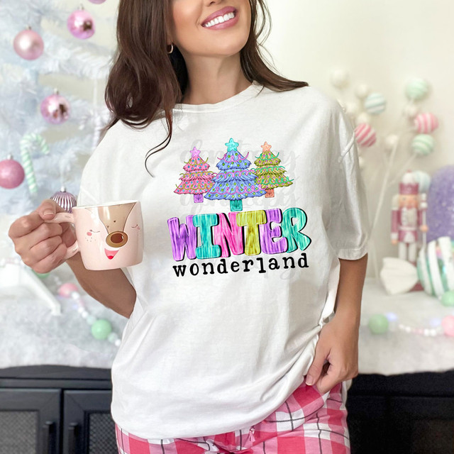 Winter Wonderland DTF Heat Transfer, colorful Christmas trees and the word 'WINTER' in vibrant letters on a white T-shirt worn by a smiling woman.