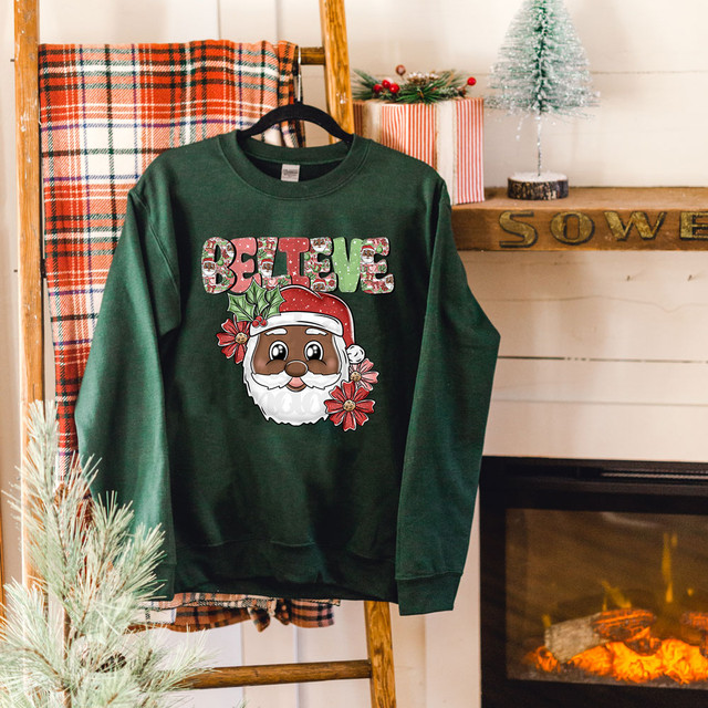 Believe Dark Skinned Santa DTF Heat Transfer, featuring a cute Santa face with festive holiday design and colorful lettering on a green sweatshirt.
