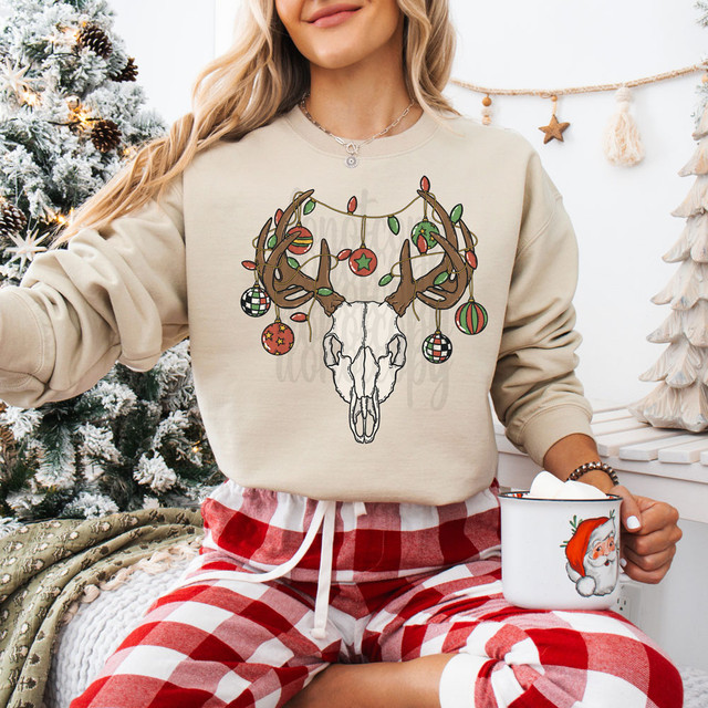 Ornament Bull Skull DTF Heat Transfer, front view of a festive sweatshirt featuring a bull skull ornament design with Christmas lights and ornaments, worn by a woman in a holiday setting.
