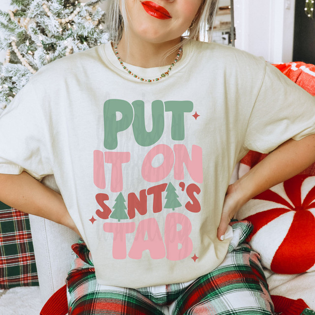Put It On Santa's Tab DTF Heat Transfer, festive graphic design with Christmas colors and themed text on a white t-shirt.
