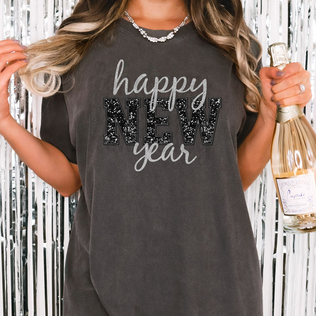 Happy New Year Faux Sequins DTF Heat Transfer, close-up of a woman wearing a dark t-shirt with festive New Year message in glittery sequins and lettering, holding a champagne bottle with a metallic background.