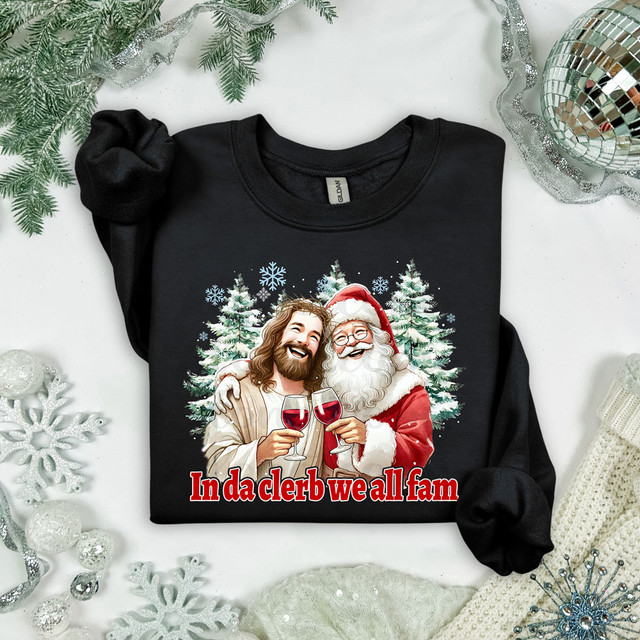 In Da Clerb We All Fam Christmas DTF Heat Transfer, black T-shirt with a festive graphic of Jesus and Santa Claus holding glasses of wine, surrounded by snowflakes and Christmas trees.