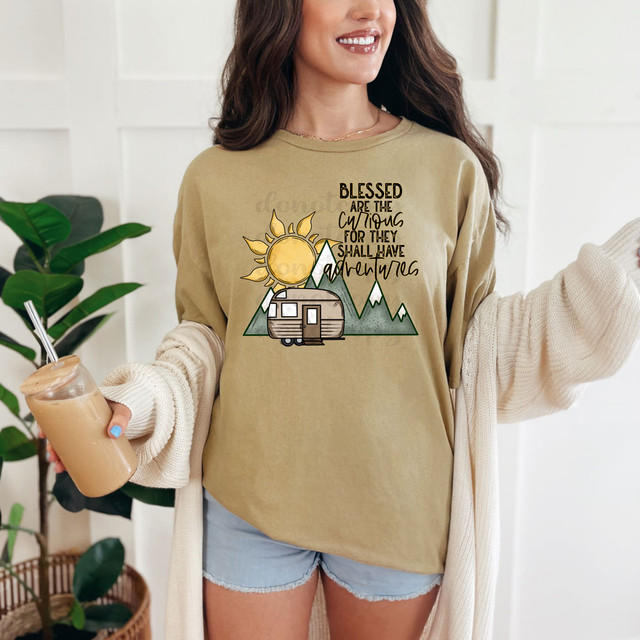 Blessed Are The Curious For They Shall Have Adventures DTF Heat Transfer, a woman wearing a beige sweatshirt with a mountain, sun, and caravan design apt for outdoor adventurers.
