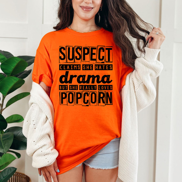 Suspect Claims She Hates Drama but She Really Loves Popcorn DTF Heat Transfer T-shirt, orange with bold black and orange text design.