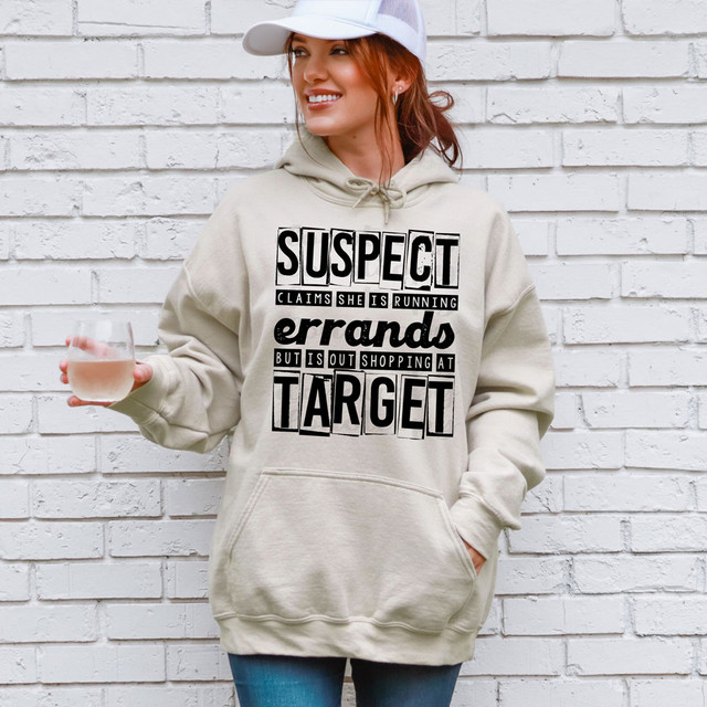 Suspect Claims She Is Running Errands But Is Out Shopping At Target DTF Heat Transfer, a woman with red hair, wearing a beige hoodie with bold black text, holding a glass of rosé wine, standing in front of a white brick wall.