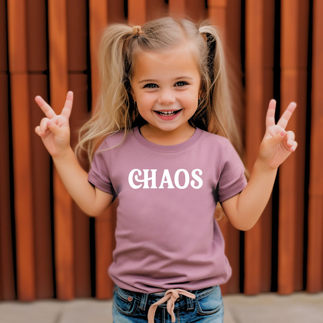 Chaos WHITE DTF Heat Transfer, a young girl with blonde hair wearing a purple t-shirt with the word 'CHAOS' printed in white, smiling and making peace signs with her hands.