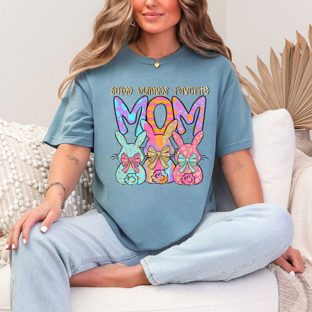 Some Bunnies Favorite Mom DTF Heat Transfer, a colorful design featuring three cute bunny illustrations with bows and the text 'Some Bunnies Favorite Mom' on a blue t-shirt.
