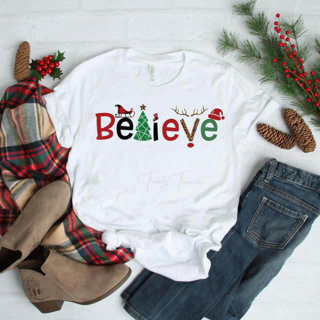 Believe Christmas T-shirt, white T-shirt with festive holiday design including Christmas tree, Santa, reindeer antlers, and holiday hat.