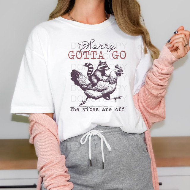 Sorry Gotta Go The Vibes Are Off DTF Heat Transfer, product image showing a white T-shirt with a humorous graphic of a raccoon and chicken and the text 'Sorry Gotta Go The vibes are off' for apparel customization.