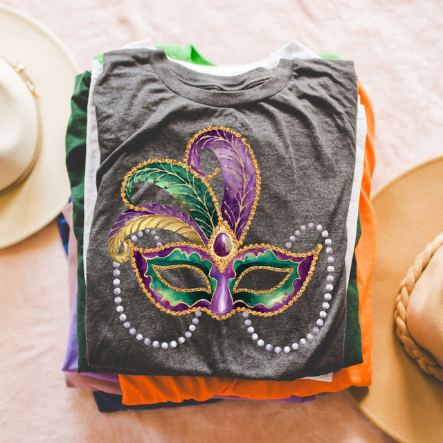 Mardi Gras Mask DTF Heat Transfer, colorful decorative mask graphic on a folded t-shirt.