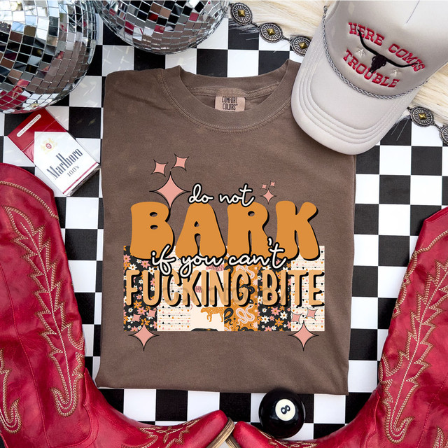 Do Not Bark If You Can't F***ing Bite DTF Heat Transfer, T-shirt with bold lettering and decorative elements, surrounded by red cowboy boots, a white cap with embroidered text, and patterned disco balls.