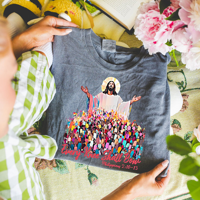Every Knee Shall Bow Jesus DTF Heat Transfer, a gray T-shirt featuring an illustration of Jesus Christ with outstretched arms and a crowd of people, with colorful text and biblical reference.
