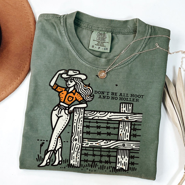 Don't Be All Hoot And No Holler DTF Heat Transfer T-Shirt, green color with graphic design of a woman in cowboy outfit leaning on a wooden fence