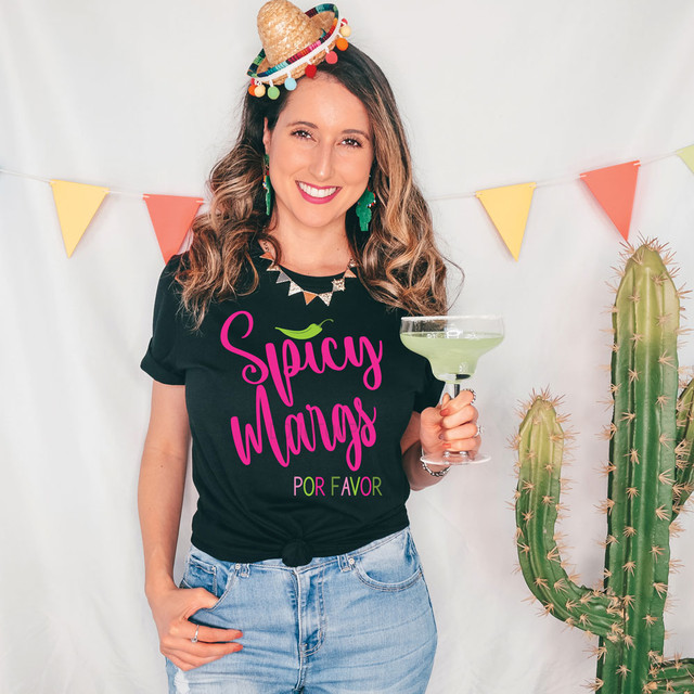 Spicy Margs Por Favor DTF Heat Transfer, colorful digital design on a black T-shirt worn by a smiling woman holding a margarita glass, vibrant party decor with cactus in the background.