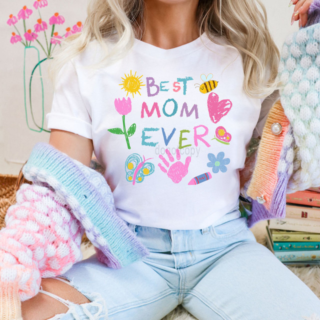 Best Mom Ever Doodle DTF Heat Transfer, colorful printed design on a white T-shirt with flowers, sun, heart, bee, butterfly, handprint, flower, lipstick, and crayon graphics.