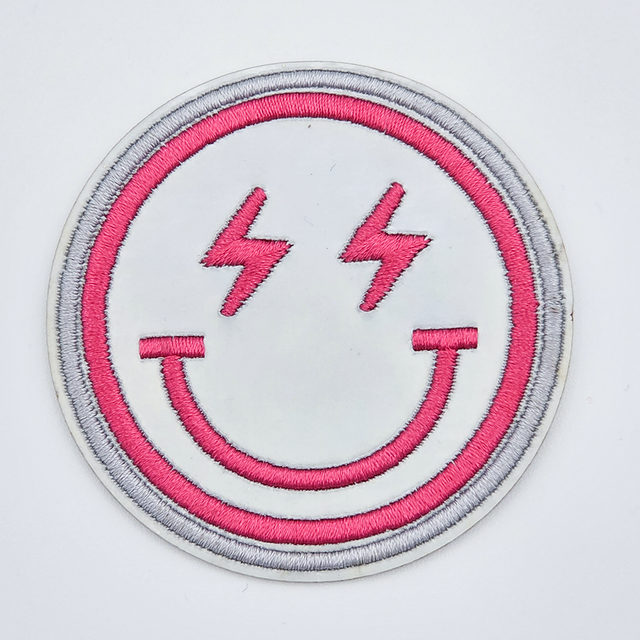 Silver Iridescent Smile Embroidered HAT/POCKET Patch, round patch featuring a pink embroidered smiling face with lightning bolt eyes and a pink outline.