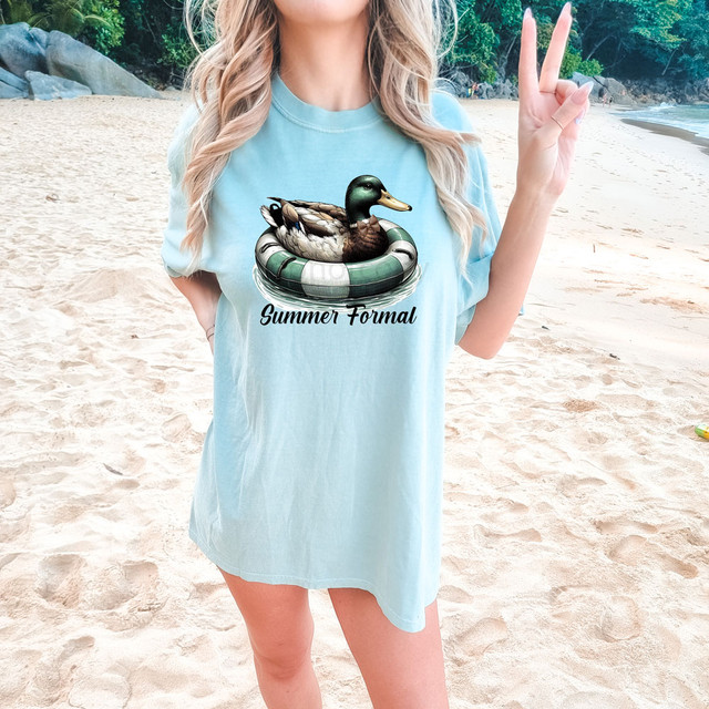 Summer Formal DTF Heat Transfer, a woman wearing a light blue T-shirt with a duck in a swim ring and the text 'Summer Formal' printed on it, on a sandy beach.