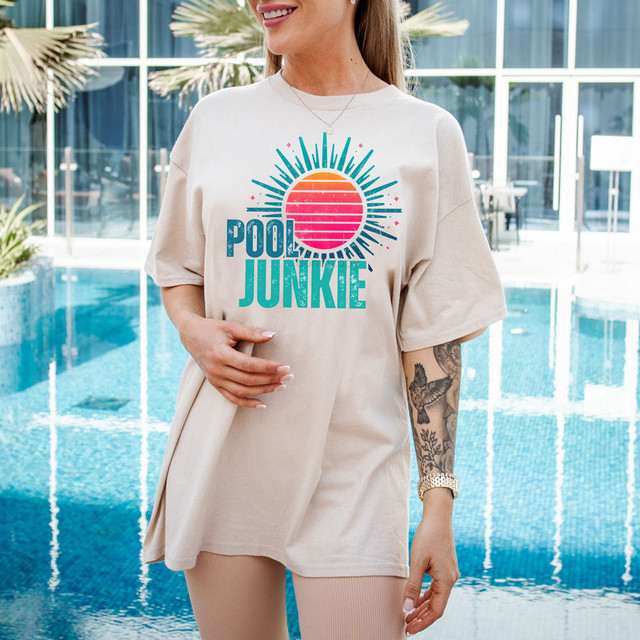 Distressed Pool Junkie DTF Heat Transfer, colorful sun with rays and Pool Junkie text on a woman's t-shirt near a swimming pool.