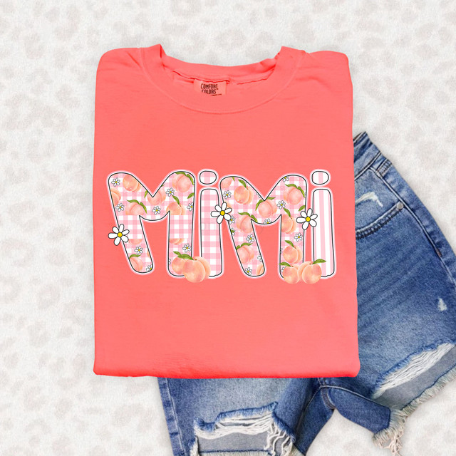 Mimi Peachy Floral Gingham DTF Heat Transfer, a pink t-shirt with the word 'Mimi' designed with peach and daisy patterns, laid over denim shorts.