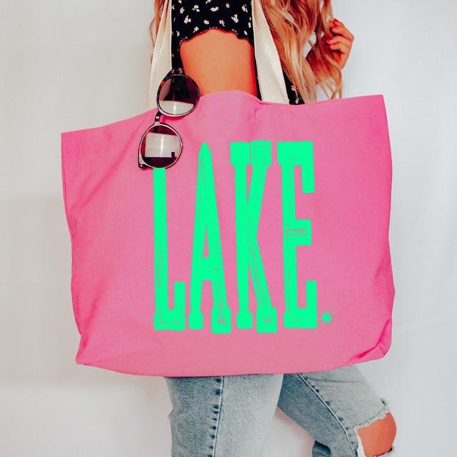 Distressed Lake DTF Heat Transfer on pink tote bag, with the word 'LAKE' in bright green, displayed on a woman carrying the bag.