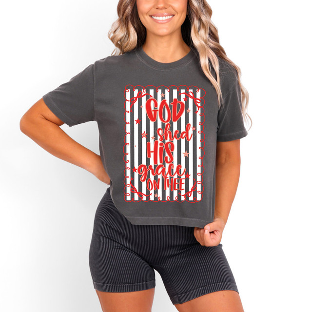God Shed His Grace On Thee DTF Heat Transfer, a colorful design with red and gray text and stars on a striped background applied on a dark gray t-shirt worn by a smiling woman.