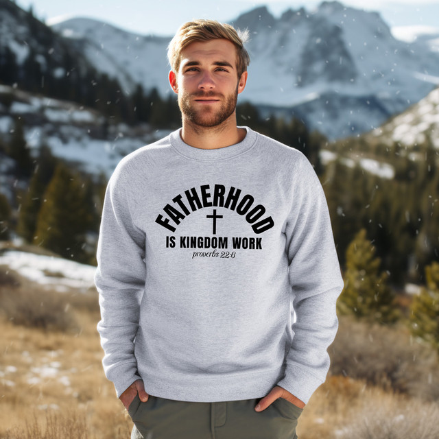 Fatherhood Is Kingdom Work BLACK DTF Heat Transfer, a man wearing a gray sweatshirt with this text printed on it, standing outdoors in a snowy mountain landscape.