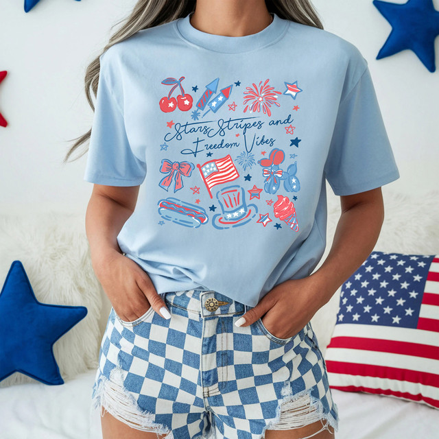 Stars, Stripes And Freedom Vibes DTF Heat Transfer, patriotic summer design on a light blue t-shirt with themed fireworks, flag, bow, ice cream, hot dog, and stars.