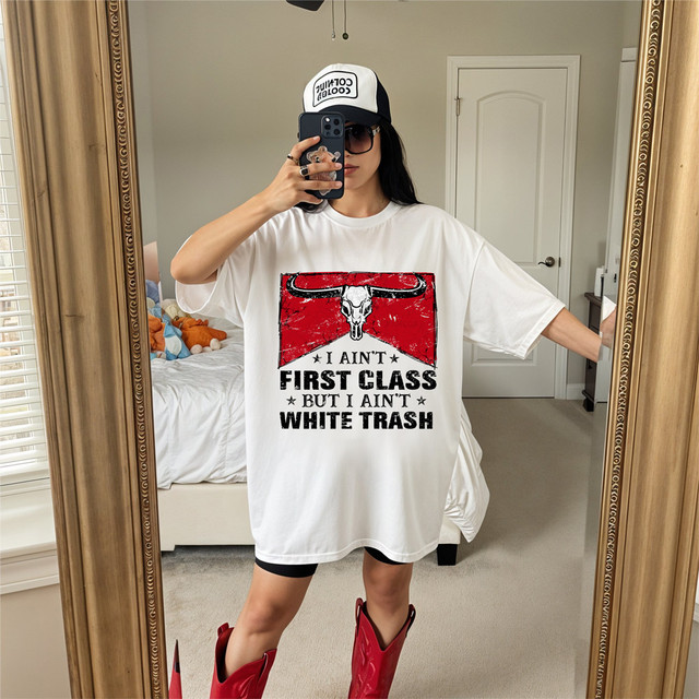 I Ain't First Class But I Ain't White Trash DTF Heat Transfer, woman wearing a white oversized t-shirt with a graphic and text, a baseball cap, sunglasses, and red cowboy boots, taking a mirror selfie in a bedroom.