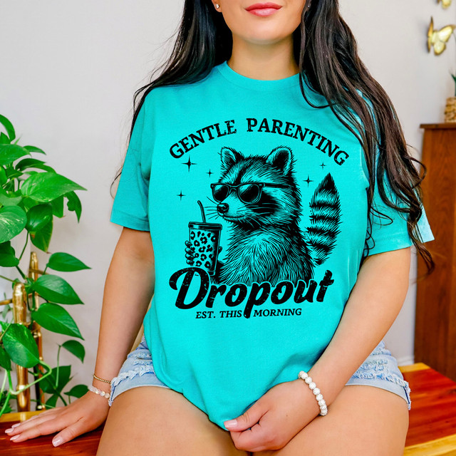 Gentle Parenting Drop Out, this morning DTF heat transfer image of a woman wearing a turquoise T-shirt with a raccoon graphic and the text 'Gentle Parenting Drop Out, Est. This Morning'.