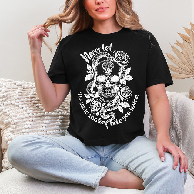 Never Let The Same Snake Bite You Twice WHITE DTF Heat Transfer, white graphic design with skull, snakes, roses, and text on a black T-shirt worn by a woman.