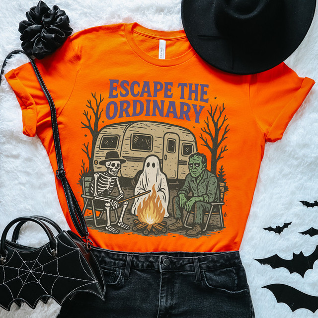 Escape The Ordinary DTF Heat Transfer, Halloween-themed orange T-shirt with skeleton, ghost, and Frankenstein graphic around a campfire, with Halloween decorations like a black hat, spider web bag, and bats.