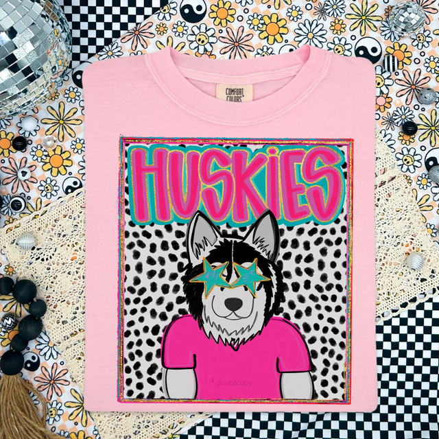Huskies Colorful Mascot DTF Heat Transfer, a vibrant design featuring a cartoon husky with star-shaped glasses on a pink shirt, with bold colorful 'HUSKIES' text and a fun polka dot background.