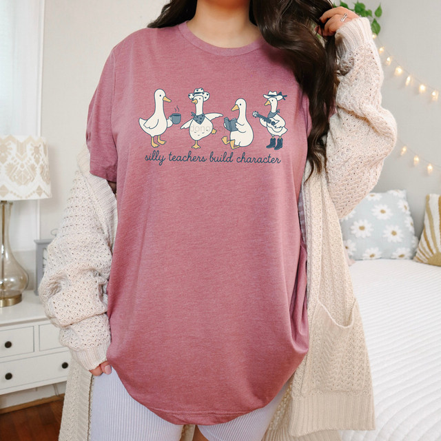 Silly Teachers Build Character DTF Heat Transfer, a pink shirt featuring cartoon teacher animals with the text 'silly teachers build character' for educational and humorous purposes.