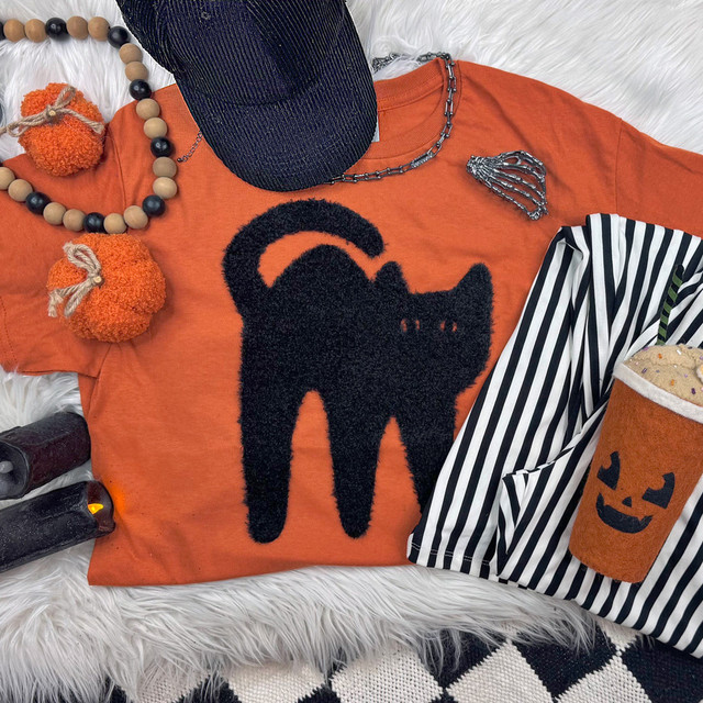 Black Cat Fluffy Patch, orange T-shirt with black fluffy cat patch, Halloween-themed accessories, pumpkin costume cup, striped clothing, black hat, Halloween jewelry, black candles