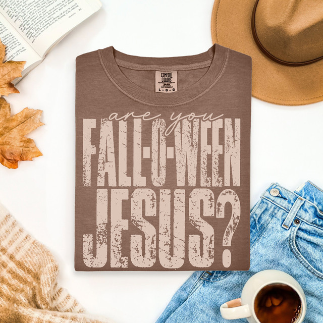 Distressed Are You Fall-O-Ween Jesus DTF Heat Transfer, Brown T-shirt with Halloween Jesus message, surrounded by autumn leaves, a cup of tea, a hat, and blue jeans.
