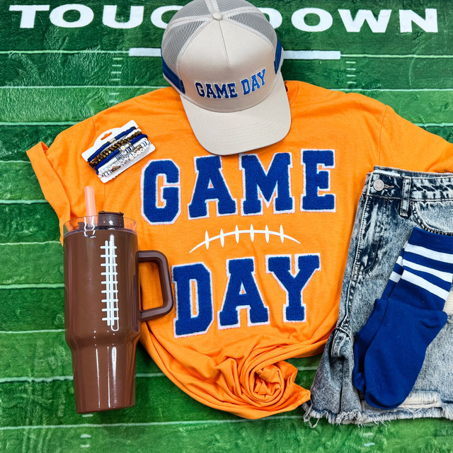 Game Day with Silicon Laces Patch - 10 Colors, sports-themed accessories, including a cap, t-shirt, water bottle, socks, and bracelets, arranged on a green football field background.