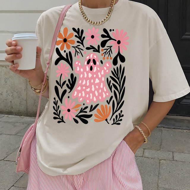 Product Floral Boho Ghost DTF Heat Transfer, a pink cartoon ghost surrounded by colorful flowers and black leaves on a white T-shirt.