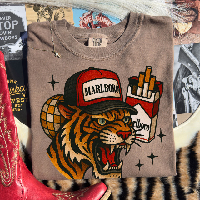 Marlboro Tiger DTF Heat Transfer, graphic design featuring a roaring tiger wearing a Marlboro cap with a pack of Marlboro cigarettes in the background, on a folded t-shirt.
