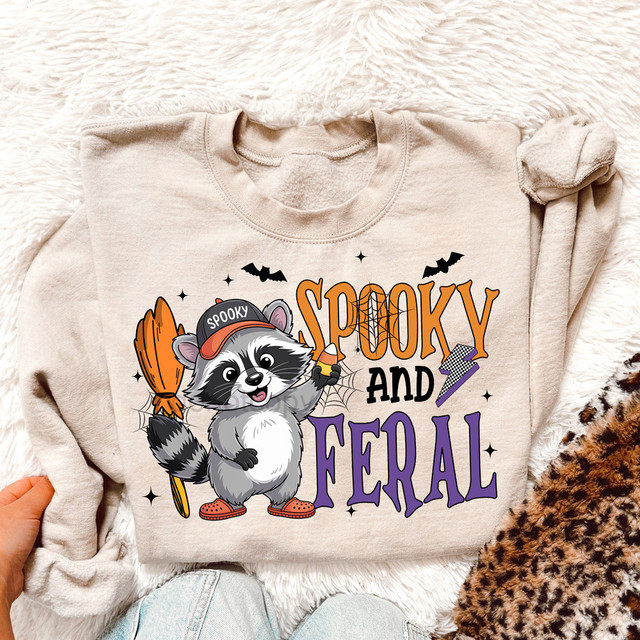 Spooky And Feral Halloween Raccoon DTF Heat Transfer, cute raccoon dressed as a witch with Halloween-themed accessories on a sweatshirt.