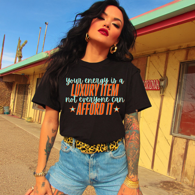 Your Energy Is A Luxury Item DTF Heat Transfer, woman wearing a black T-shirt with motivational quote and casual denim shorts standing outdoors.