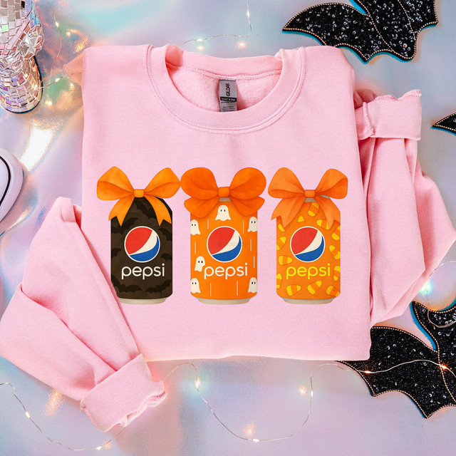 Pepsi Halloween Cans DTF Heat Transfer, pink sweatshirt with three Halloween-themed Pepsi can designs featuring orange bows and festive patterns.