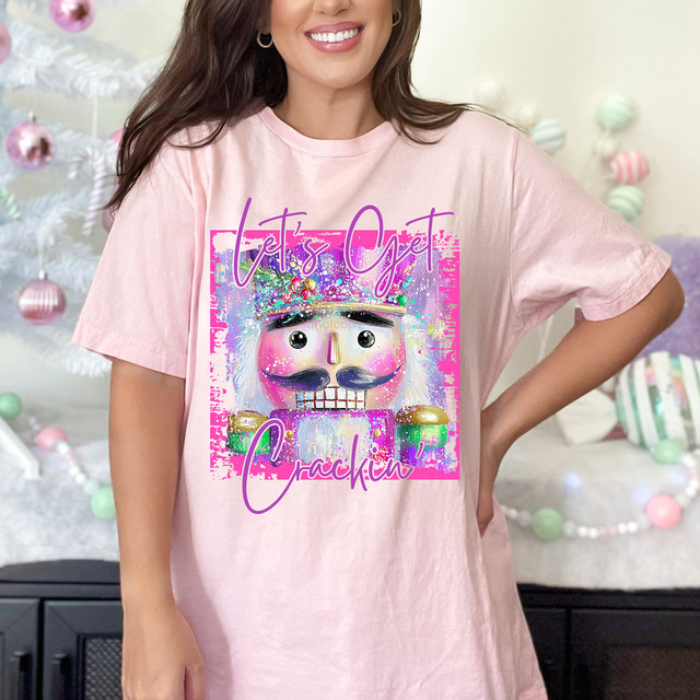 Let's Get Crackin' Nutcracker DTF Heat Transfer, colorful cartoon nutcracker with a mustache and sparkling crown, on a pink T-shirt.