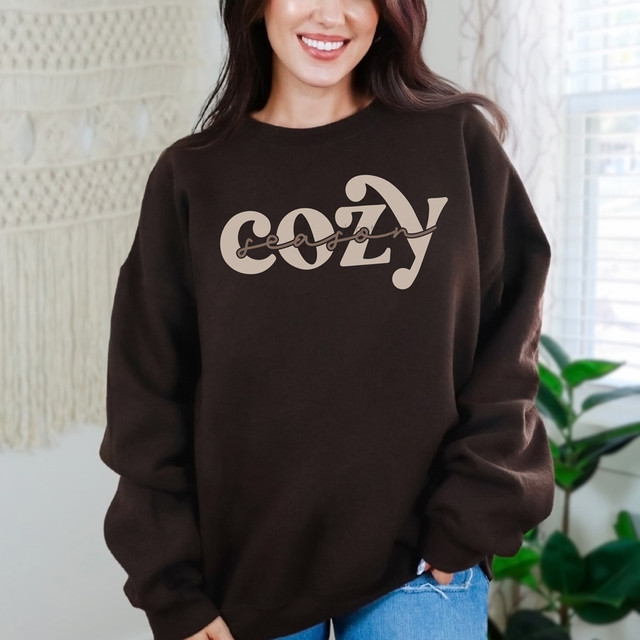 Cozy Season Script DTF Heat Transfer, close-up of a woman wearing a black sweatshirt with the beige 'cozy' script design heat transfer on the front.