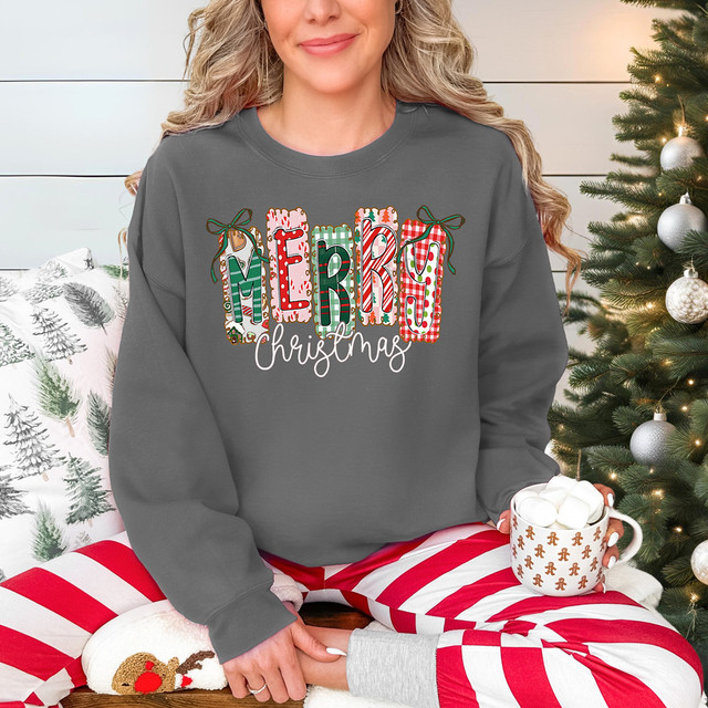 Merry Christmas Pattern WHITE DTF Heat Transfer, festive Christmas sweater with colorful gift box designs spelling 'MERRY Christmas' on a woman in holiday pajamas near a Christmas tree.