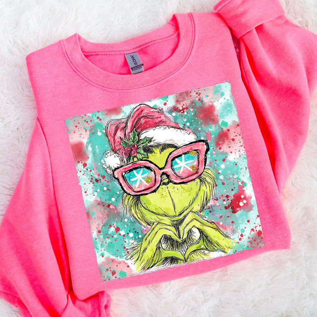 Green Guy Heart Hands DTF Heat Transfer, colorful and festive design on a pink sweatshirt featuring a cartoon character wearing a Santa hat, pink sunglasses, and making a heart sign with its hands.